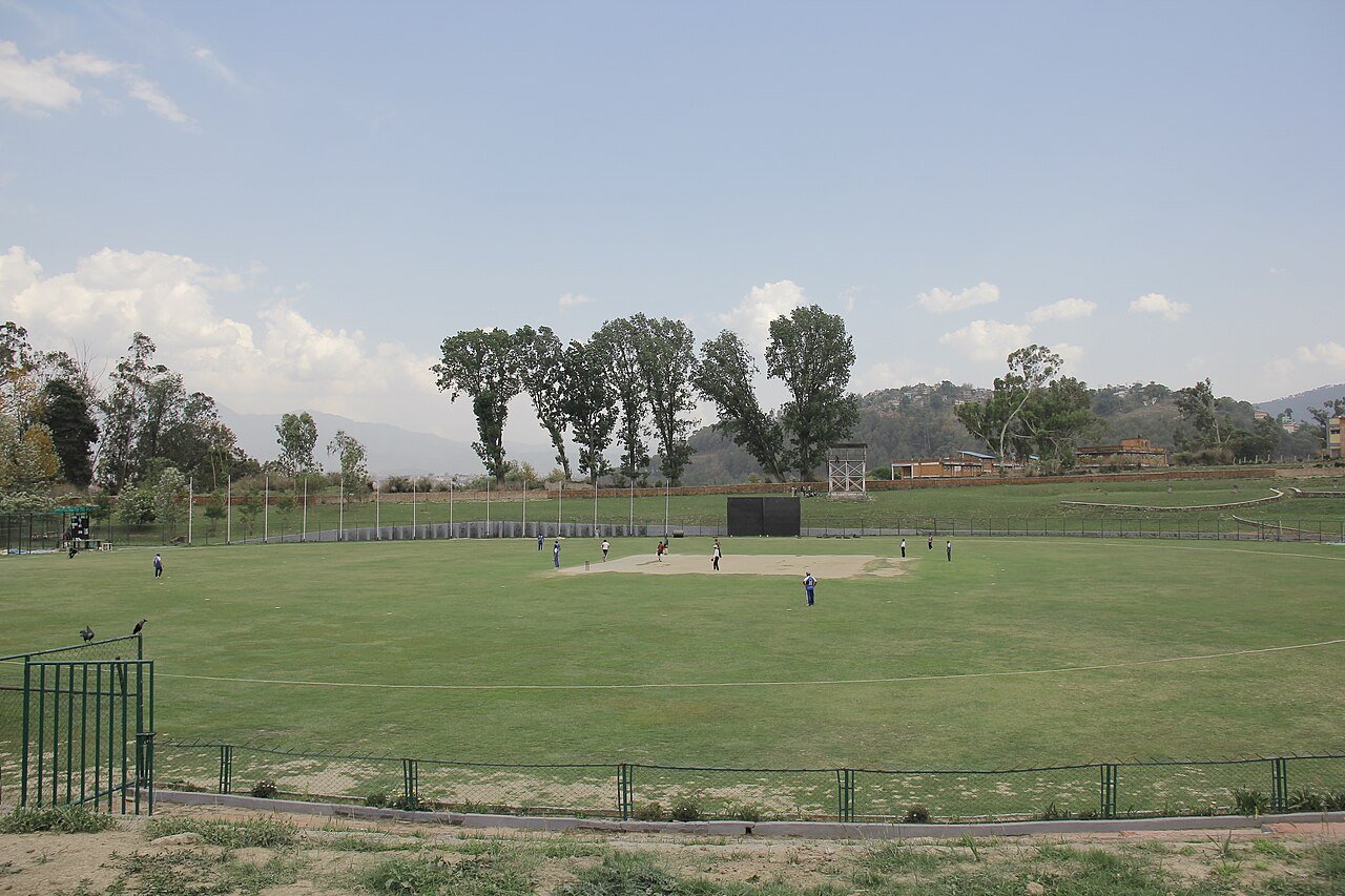 A wide view over the grass and pitch at Kirtipur Cricket Ground