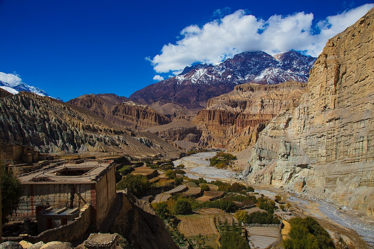 Terraced fields and earthen buildings beneath mountain cliffs in Lower Mustang