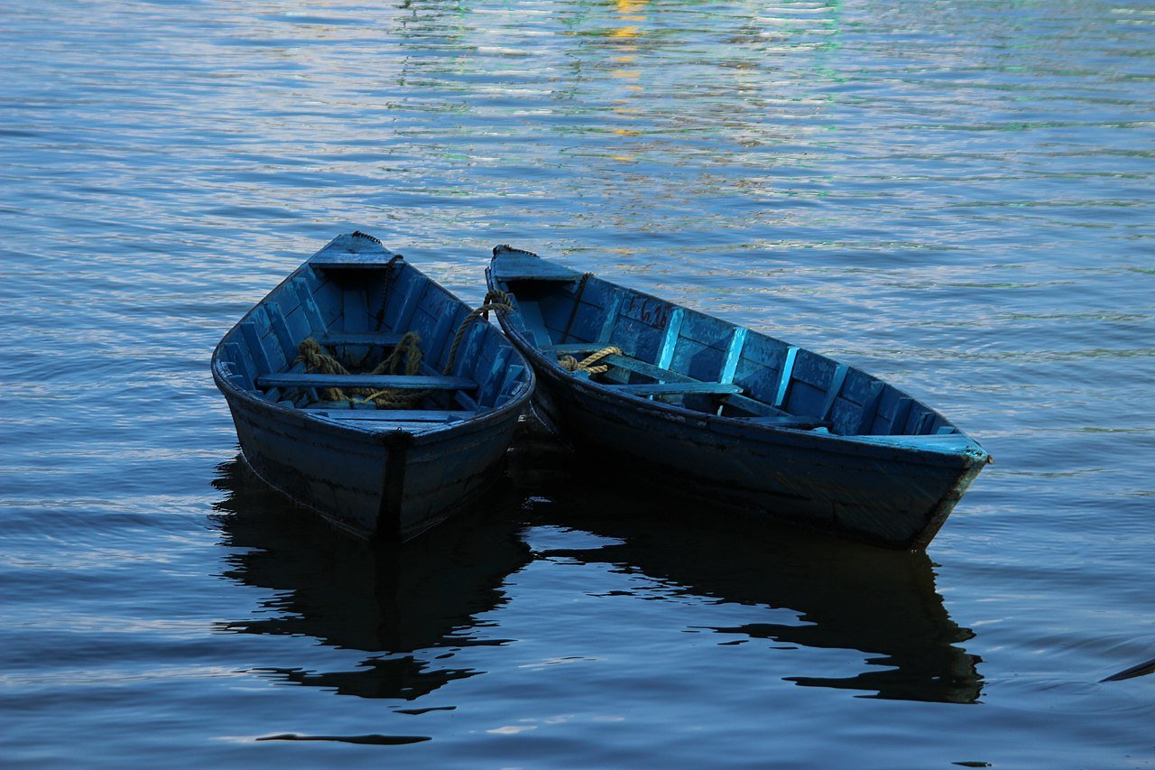 Two blue wooden canoes floating on Phewa Lake in Pokhara